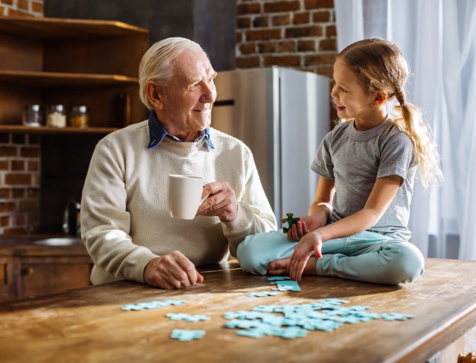 Joyful aged man assembling jigsaw puzzles with his granddaughter